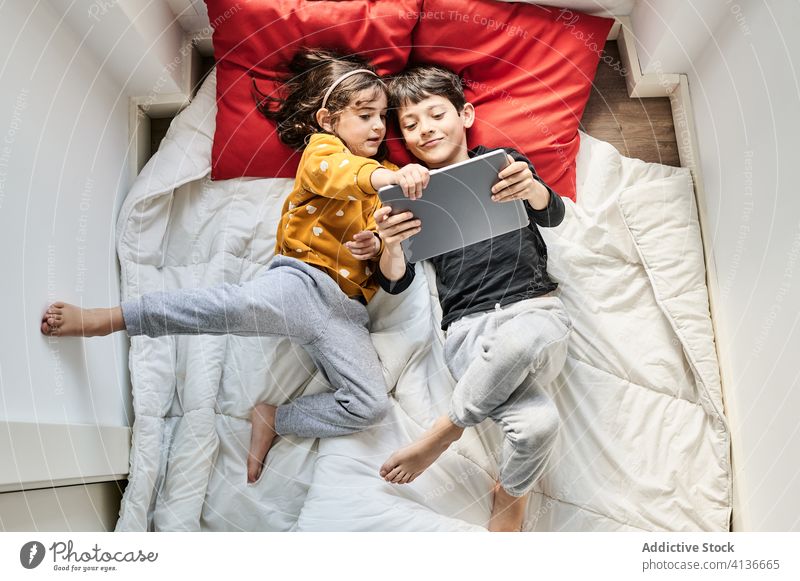 Freundliche Geschwister benutzen gemeinsam ein Tablet auf einer Decke Geschwisterkind benutzend Tablette zuschauen Karikatur Schwester Bruder Lügen unterhalten