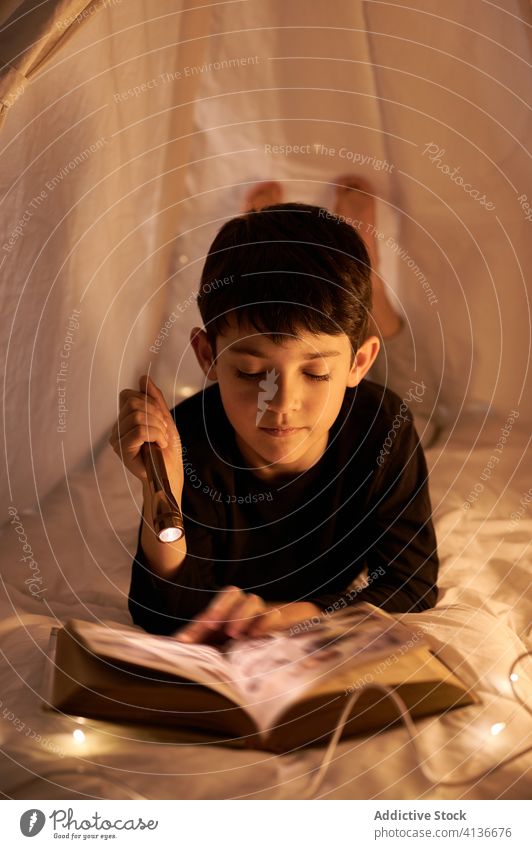Konzentrierter Junge liest Märchen im Kinderzelt zu Hause Zelt Buch lesen Taschenlampe Freizeit Literatur konzentriert Kindheit heimwärts Windstille Lügen