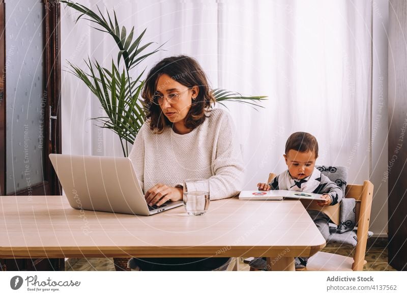 Mutter arbeitet mit Laptop am Tisch mit Kind Frau Arbeit heimwärts benutzend beschäftigt online abgelegen modern jung Zusammensein Baby Internet Browsen Gerät