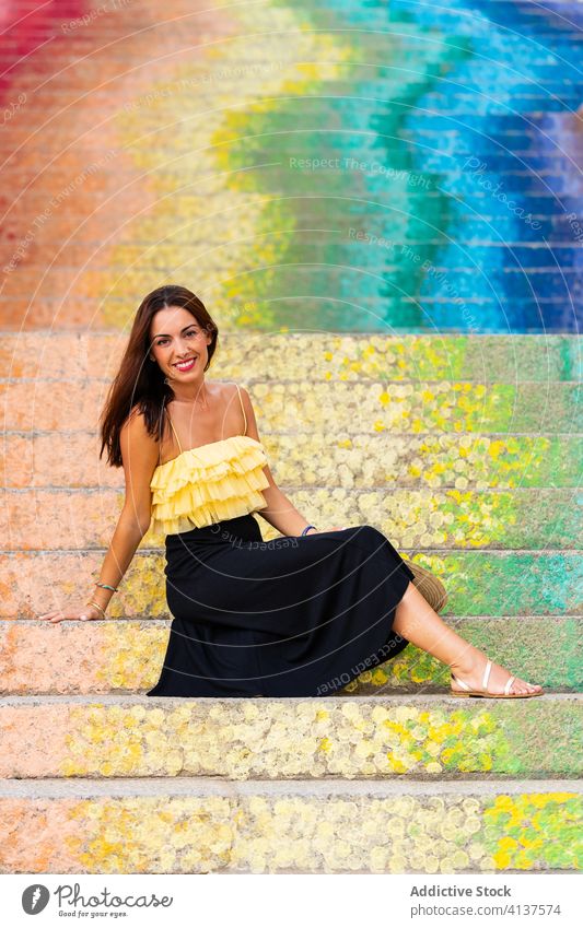 Lächelnde Frau auf bunten Stufen Sommer Urlaub Großstadt Reisender farbenfroh Regenbogen Schritt Treppe Straßenkunst heiter Tourist sitzen Glück Freude
