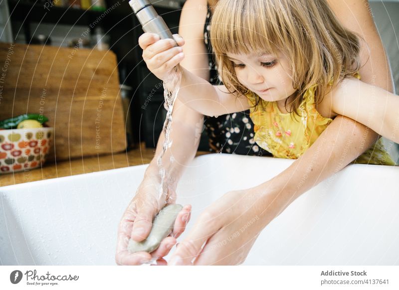 Mutter und Tochter beim Umgang mit dem Wasserhahn interagieren Waschbecken Waschen Hand lehren Küche heimwärts Umarmung Umarmen wenig Lifestyle Kindheit