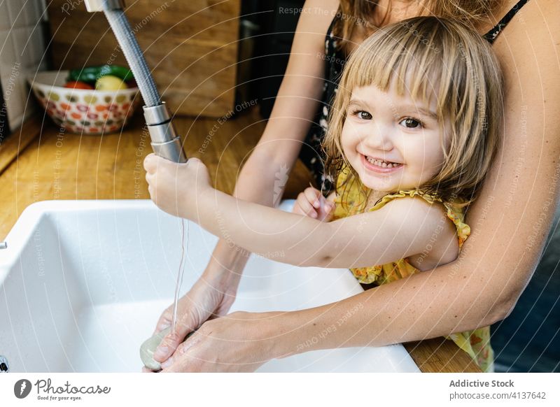Fröhliches Mädchen beim Händewaschen mit der Mutter Tochter Waschen Hand Seife Lächeln lehren Küche heimwärts Waschbecken Wasserhahn Umarmung Umarmen wenig