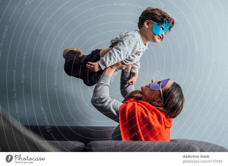 Lächelnde Mutter spielt mit Sohn zu Hause spielen Superheld werfen Mundschutz Spiel Spaß haben Junge Zusammensein so tun, als ob kreativ spielerisch heiter