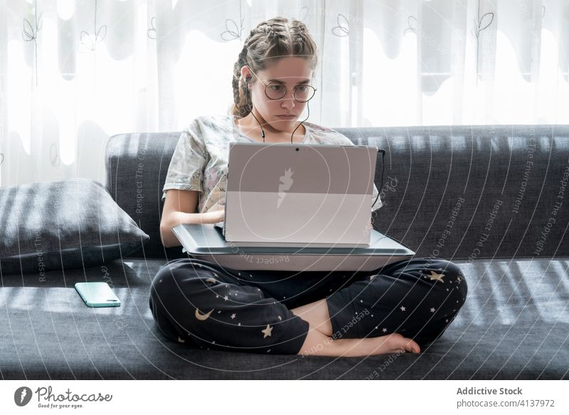 Junge Frau mit Kopfhörern am Laptop zu Hause heimwärts benutzend jung zuhören zuschauen Apparatur online Schüler lässig Video Gerät Internet Browsen Lifestyle