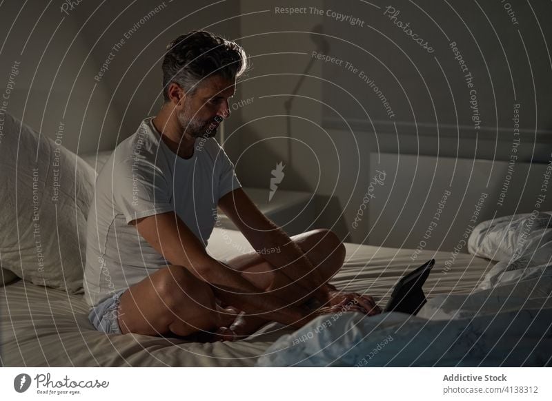 Mann benutzt Laptop im Schlafzimmer heimwärts Bett Browsen benutzend positiv reif Sitzen ruhen männlich lässig Gerät Apparatur sich[Akk] entspannen online