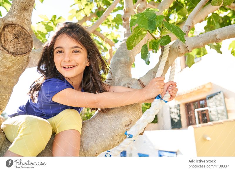 Kleines Mädchen sitzt auf einem Baum und bereitet sich auf einen Sprung mit dem Seil vor Kind Spaß haben Sommer Aktivität Glück Urlaub Feiertag positiv Garten