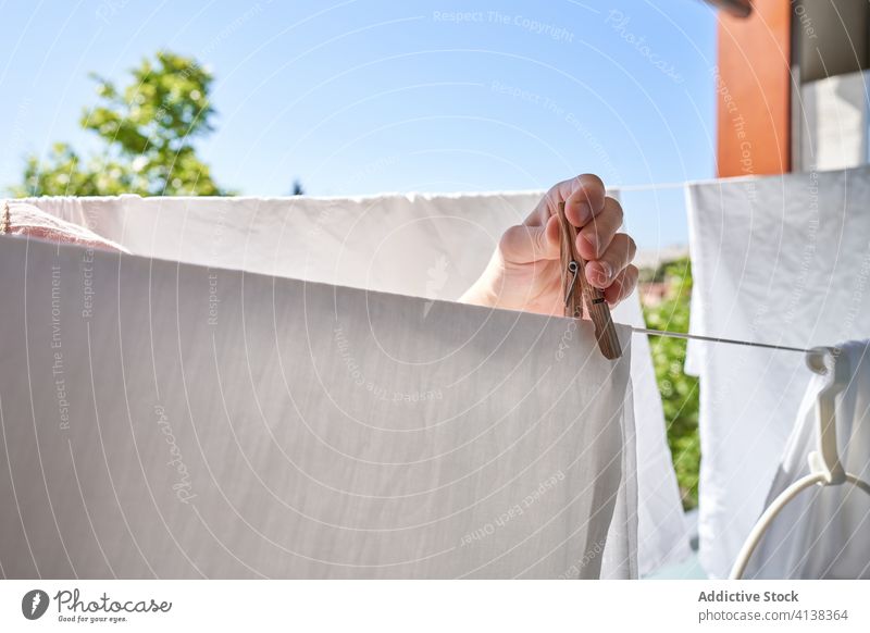 Nicht erkennbare Person, die mit Heringen am Seil hängende Kleidung auf dem Balkon Wäscherei Kleiderspin Leinen nass trocknen Sonnenlicht Sommer heimisch Arbeit