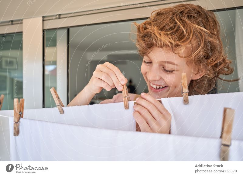 Junge auf Balkon und Wäsche aufhängen Kind Leinen heimisch Wäscherei Seil Arbeit Stoff Hausarbeit heimwärts verantwortlich klug Lächeln gesamt Appartement
