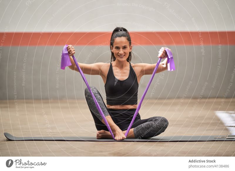 Flexible Sportlerin beim Training mit Gummiband im Fitnessstudio widersetzen Band elastisch Dehnung beweglich Übung Frau heiter Sportkleidung Barfuß Unterlage