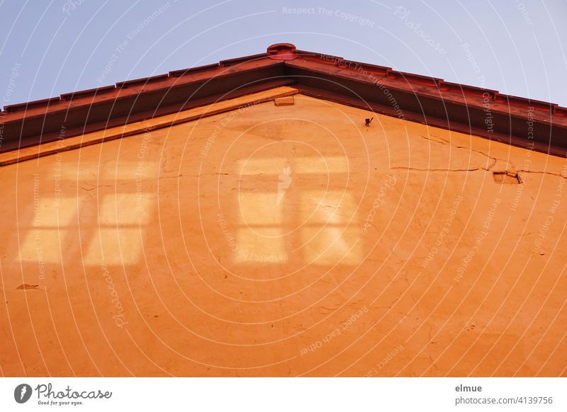 An dem orangefarbenen Hausgiebel ist das reflektierte Licht der gegenüberliegenden Fenster zu sehen / Illusion Lichtreflektion Sinnenwahrnehmung Giebel