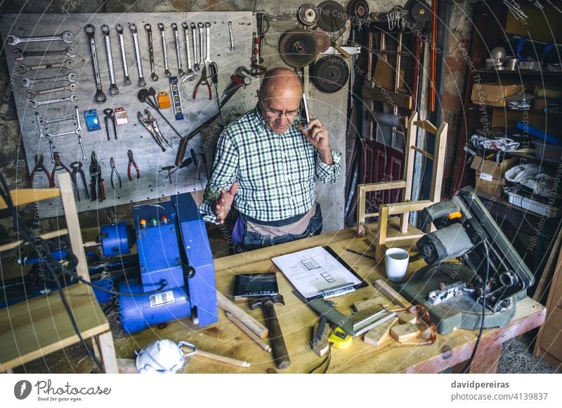 Schreiner in seiner Werkstatt Draufsicht Zimmerer Mann Mobile Senior sprechend Business maßgefertigt Werkbank reif Tablette männlich Schreinerei schreibend Holz