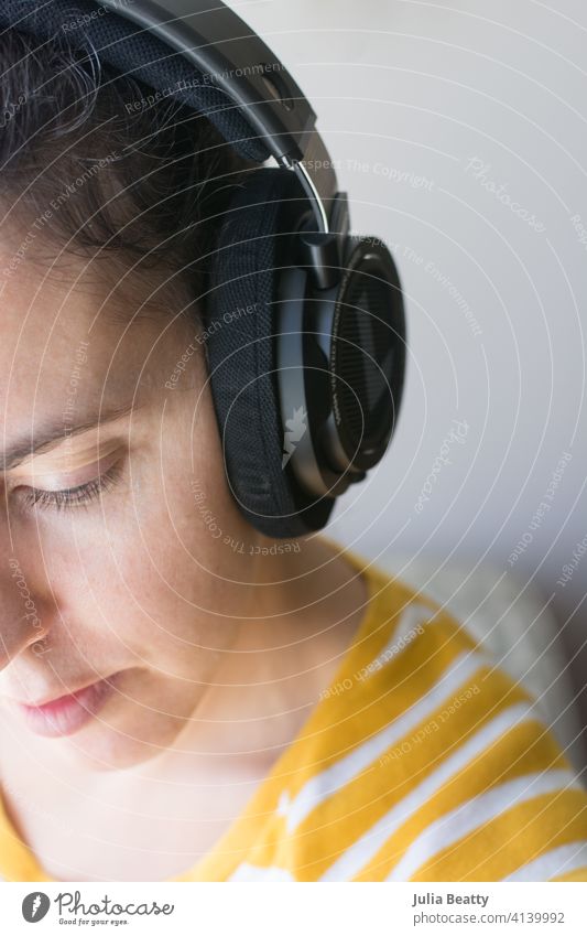 Frau mit Kopfhörern, die einen Podcast oder Musik hört; weiblich, Anfang 40, mit gestreiftem Hemd zuhören Audio Hörbuch Konzentration Training Fernarbeit