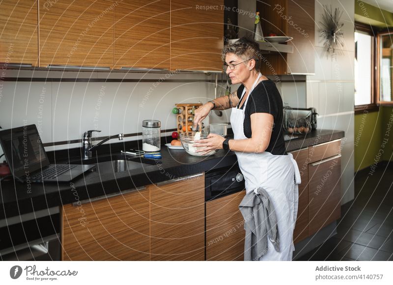 Frau mittleren Alters kocht in der Küche Hausfrau Koch mischen Bestandteil zuschauen Film Rezept Laptop benutzend Lebensmitte vorbereiten Gebäck