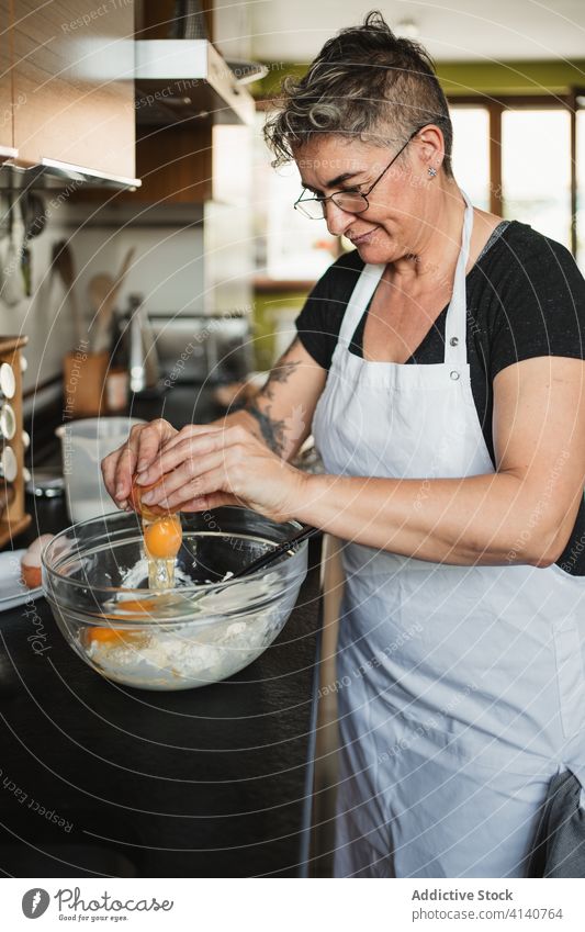 Reife Frau beim Kochen in der Küche vorbereiten Teigwaren Hausfrau Gebäck hinzufügen Ei Bestandteil Mehl Schalen & Schüsseln reif Lebensmitte Tisch kulinarisch