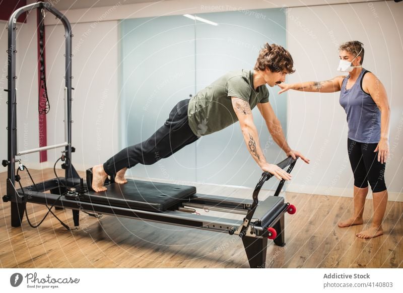 Sportler an einem Pilates-Gerät unter Aufsicht einer Trainerin Reformer Übung üben Training Zusammensein Coronavirus Fitnessstudio Maschine Atemschutzgerät