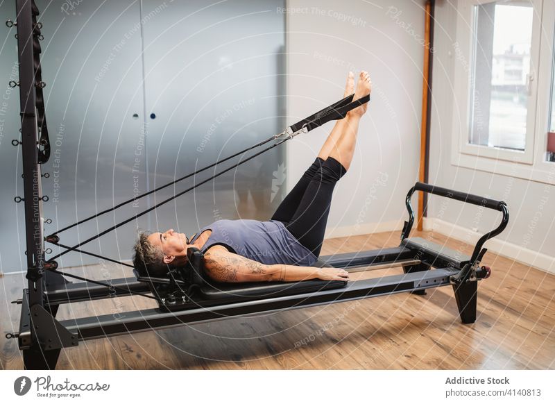 Flexible Frau bei Übungen auf dem Pilates-Reformer Maschine Sportlerin Training Dehnung beweglich Fitnessstudio widersetzen Band Sportbekleidung Lügen modern