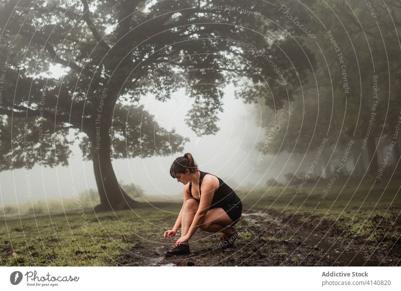 Sportlerin beim Binden von Schnürsenkeln beim Training im Wald Krawatte Schuhbänder passen Nebel Wälder Turnschuh Pause Frau Sportbekleidung Athlet Fitness