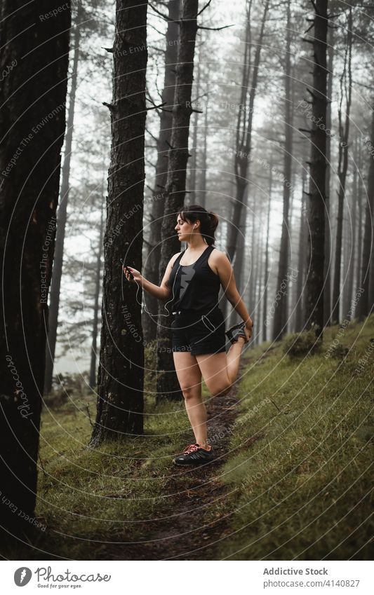 Weibliche Läuferin hört Musik im nebligen Wald zuhören Frau Smartphone müde Pause benutzend Training Wälder Nebel eng Sportkleidung Sportlerin Weg Gesundheit