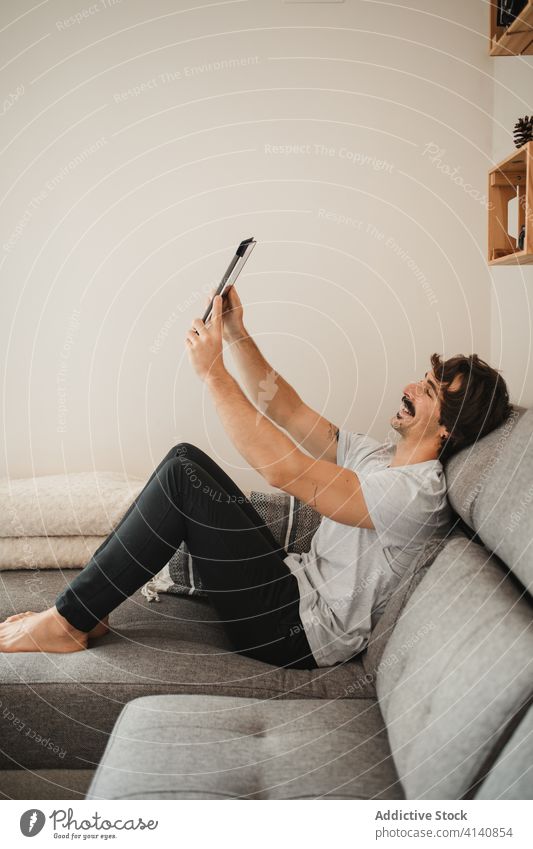 Zufriedener Mann im Videochat über ein Tablet Videoanruf heimwärts Tablette Video-Chat reden Gruß gestikulieren sprechen männlich sich[Akk] entspannen