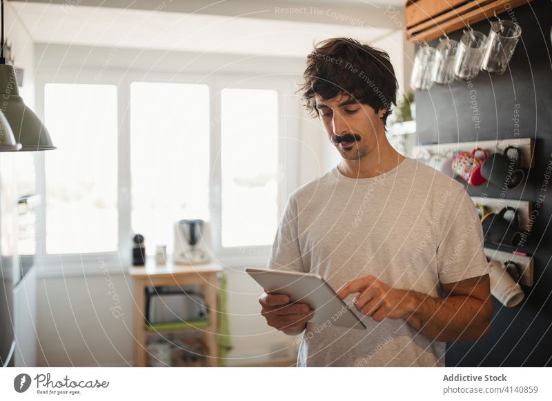 Mann benutzt Tablet in der Küche Tablette Browsen modern heimwärts ernst benutzend Gerät lässig Internet männlich Surfen Anschluss online Kommunizieren
