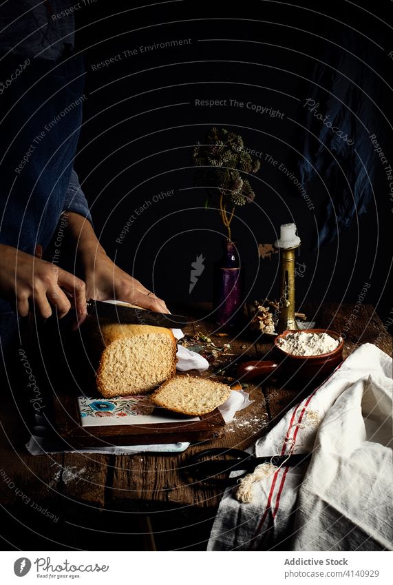 Anonyme Person schneidet Brot und Hüttenkäse auf dem Tisch Brotlaib rustikal dunkel selbstgemacht Quark Küche Leuchter Vase Pflanze Schalen & Schüsseln