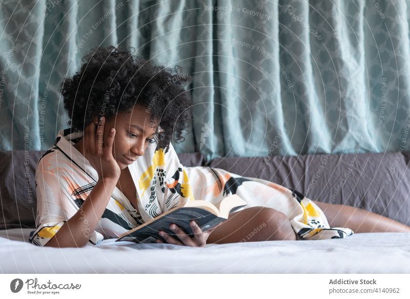 Konzentrierte ethnische Frau liest zu Hause ein Buch lesen genießen heimwärts Roman ruhen Komfort Bett Inhalt schwarz Afroamerikaner Lügen Seide Robe