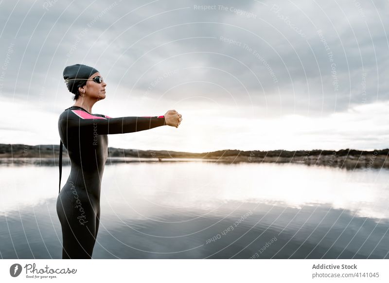 Ruhige Frau streckt sich auf Felsen am Seeufer Dehnung Natur Aufwärmen Taucher Neoprenanzug Harmonie Windstille bedeckt Wassersport Sport Wellness beweglich