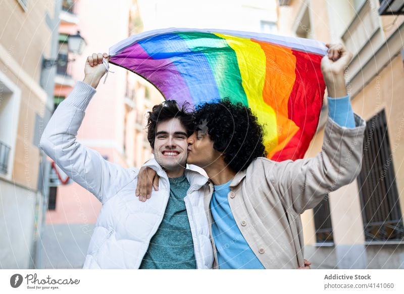 Liebendes schwules Paar mit LGBT-Flagge lgbt Fahne Kuss Straße Toleranz Partnerschaft Homosexualität Regenbogen vielfältig rassenübergreifend ethnisch Zuneigung