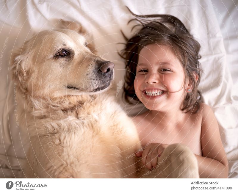 Glückliches Mädchen liegt mit Hund auf zerknittertem Bettlaken ruhen Zuneigung Begleiter Zahnfarbenes Lächeln Zusammensein idyllisch heimwärts Harmonie Schot