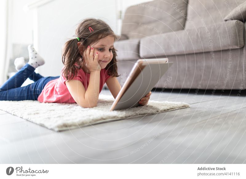 Kleines Mädchen benutzt mit Vergnügen ein digitales Tablet, während es zu Hause entspannt Tablette heimwärts Kälte Kind zuschauen lesen Eltern Glück
