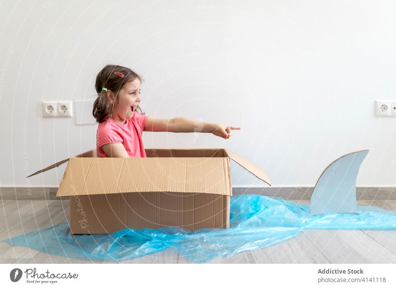 Fröhliches kleines Mädchen in Pappkarton segelt vom Hai weg Haifisch Boot Paddel Spiel Vorstellungskraft Spaß spielerisch Kind Kasten spielen Matrosen heimwärts