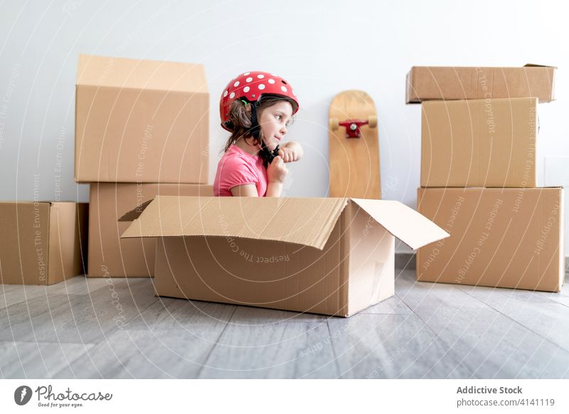 Fröhliches Mädchen spielt in Kartonschachtel spielen Kasten Lächeln Schutzhelm befestigen sitzen bewegend verlegen Spaß Vorstellungskraft Kind Phantasie Glück