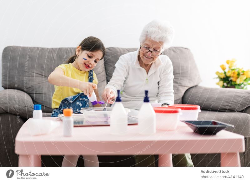 Fröhliche Großmutter und Mädchen, die zu Hause Schleim in einem Behälter herstellen Enkelin Kunsthandwerk Spaß diy Handwerk Kinderbetreuung Erziehung Vorschule