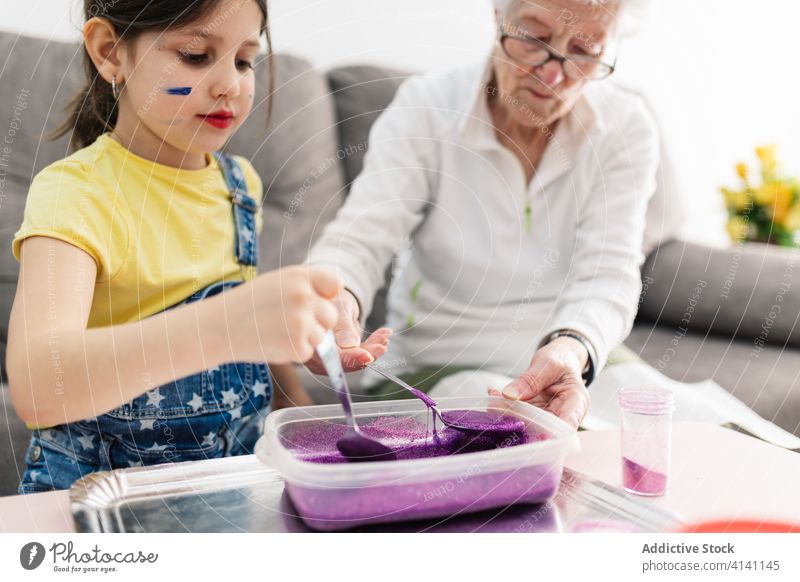 Fröhliche Großmutter und Mädchen, die zu Hause Schleim in einem Behälter herstellen Enkelin Kunsthandwerk Spaß diy Handwerk Kinderbetreuung Erziehung Vorschule