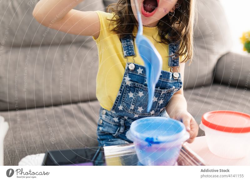 Zufriedenes Mädchen bei der Zubereitung einer bunten Schleimmischung in einem Behälter zu Hause schlank diy Prozess mischen kreativ Handwerk heimwärts rühren