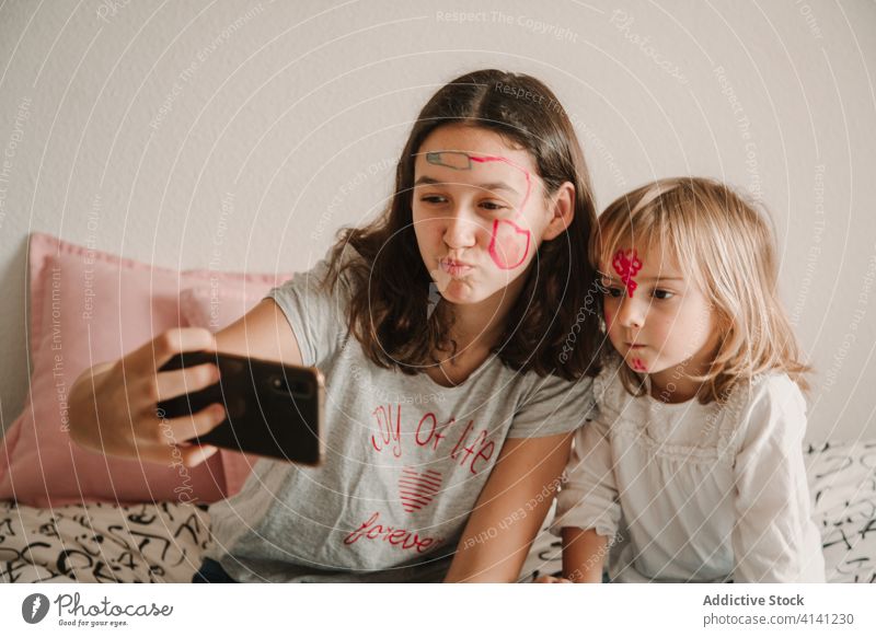 Schwestern mit bemalten Gesichtern machen Selfie mit Smartphone unterhalten Geschwisterkind Mädchen spielen benutzend wenig Teenager heimwärts Spaß haben Farbe