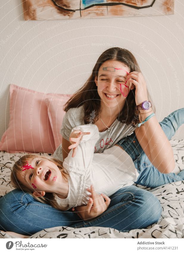 Schwestern mit bemalten Gesichtern kuschelnd auf dem Bett Lachen Spaß haben Wochenende genießen Mädchen Teenager wenig kreativ Farbe heiter Kind lässig Kindheit