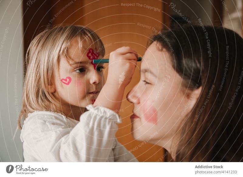 Bezaubernde Schwestern mit bemalten Gesichtern zu Hause Farbe Zeitvertreib heimwärts Mädchen Geschwisterkind Spaß haben Zusammensein spielerisch Partnerschaft