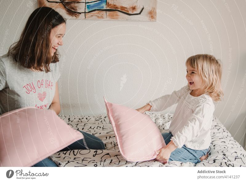 Vergnügte Schwestern kämpfen mit Kissen auf dem Bett Kopfkissen spielerisch Spaß haben spielen Spiel Mädchen Geschwisterkind wenig Teenager gemütlich