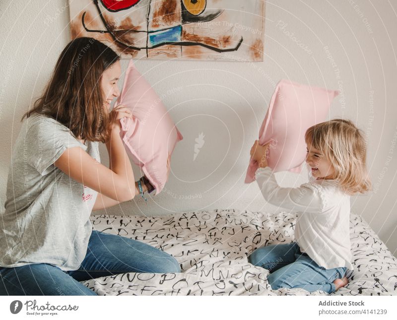 Vergnügte Schwestern kämpfen mit Kissen auf dem Bett Kopfkissen spielerisch Spaß haben spielen Spiel Mädchen Geschwisterkind wenig Teenager gemütlich
