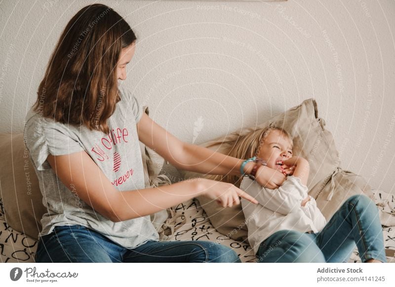 Teenager-Mädchen kitzelt kleine Schwester auf dem Bett Kribbeln Lachen spielen spielerisch Spaß haben Spiel Wochenende Zusammensein heiter heimwärts Glück
