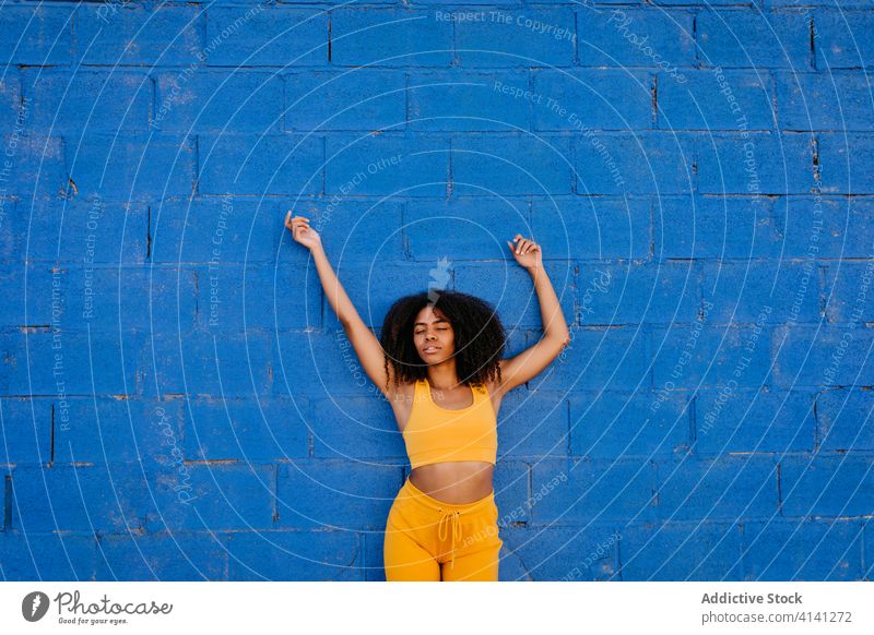 Verträumte afroamerikanische Frau, die sich auf der Straße an eine Wand lehnt verträumt Wachtraum Afro-Look Farbe lebhaft pulsierend ruhig Steinwand ethnisch