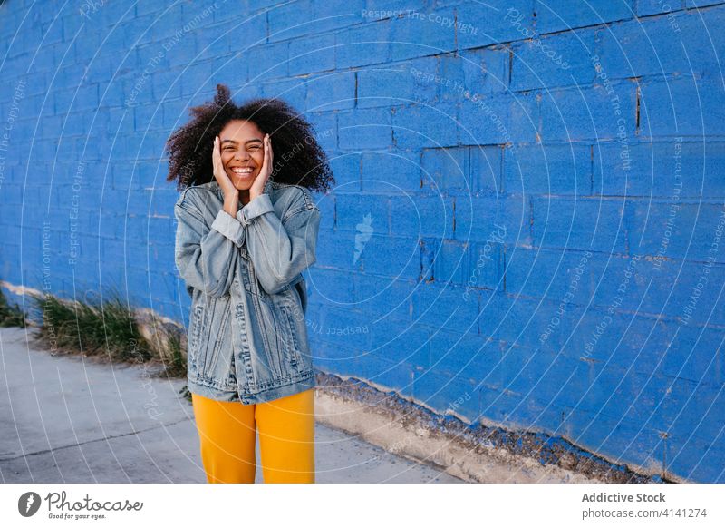 Fröhliche Frau lächelt und schneidet Grimassen auf der Straße Lächeln heiter Afro-Look Jeansstoff tausendjährig Großstadt lebhaft hell schwarz Afroamerikaner
