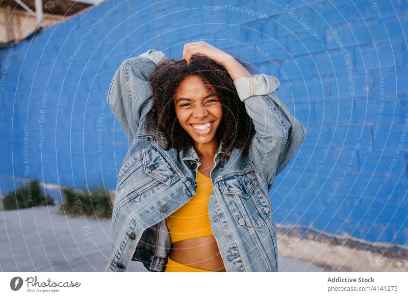Fröhliche Frau lächelt und schneidet Grimassen auf der Straße Lächeln heiter Afro-Look Jeansstoff tausendjährig Großstadt lebhaft hell schwarz Afroamerikaner