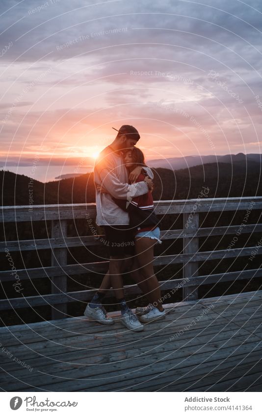 Verliebtes modernes Paar auf hoher Terrasse am Meeresufer im Licht des Sonnenuntergangs Umarmung Schiffsdeck romantisch Ufer Liebe Harmonie Berge u. Gebirge