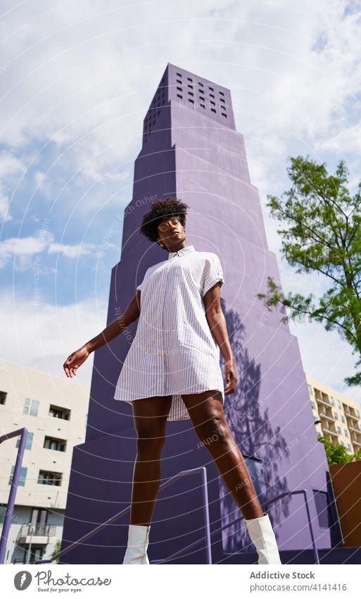 Stylish schwarze Frau posiert auf der Straße gegen lila Hochhaus in der Innenstadt Kleid Mode trendy Outfit Architektur Stil hoher Anstieg Straßenlaterne urban