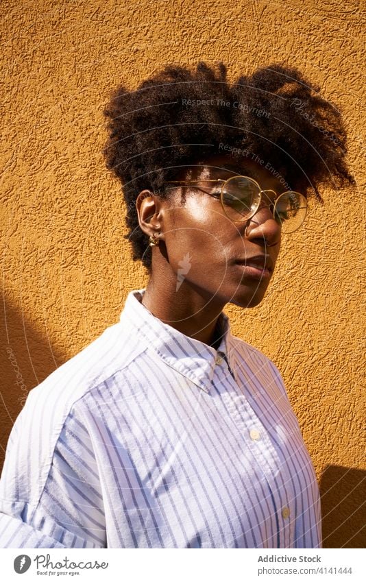 Stilvolle, nachdenkliche schwarze Frau an einem sonnigen Tag auf der Straße Persönlichkeit trendy farbenfroh Afro-Look ruhig besinnlich Brille Windstille