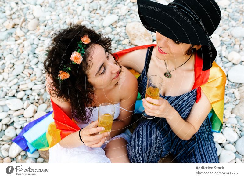 Glückliche homosexuelle Frauen, die sich umarmen und Getränke trinken lesbisch Paar Champagne lgbt Fahne Strand Klirren Regenbogen Toleranz gleich Zusammensein
