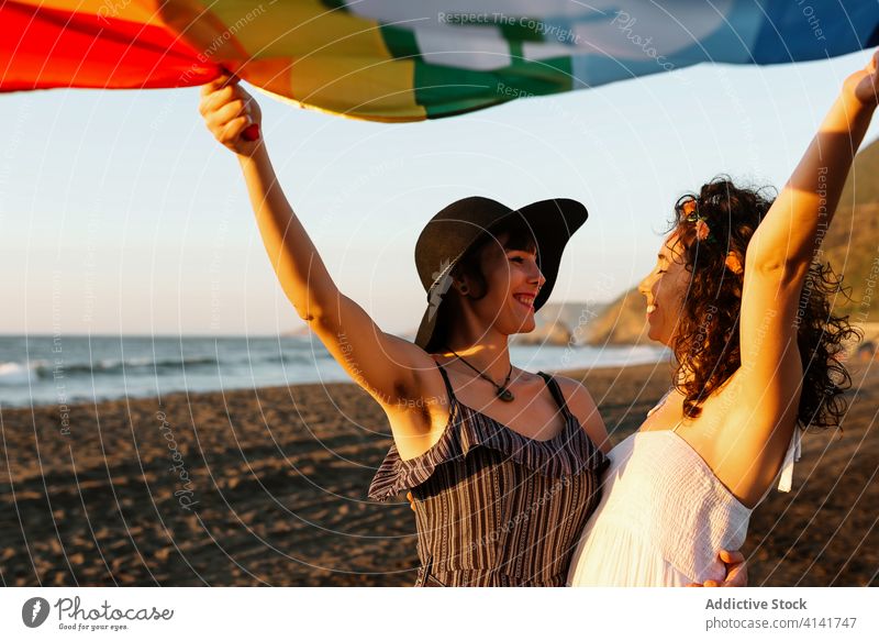 Glückliche Frauen, die eine mehrfarbige Flagge am Strand hissen Stolz Fahne Freundin lgbt lesbisch Urlaub Meer Freiheit Wochenende Homosexualität