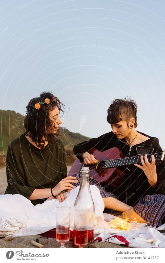 Frau spielt Gitarre für Freundin am Strand lesbisch Paar spielen Picknick Musik akustisch Sonnenuntergang lgbt Seeküste Instrument Zusammensein Musiker